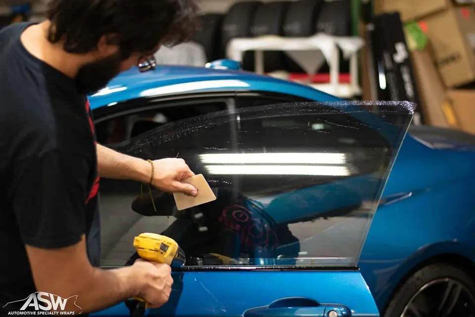 Installer heat-forming window film on a blue car